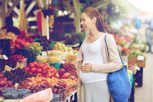 Gestante feliz e ecolhendo alimentos na feirinha